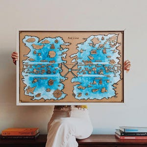 Peut inclure: Une carte encadrée avec un cadre blanc, sur le thème nautique. La carte a un fond beige avec de l'eau bleue et des masses terrestres marron. Le texte "Red Line" est visible. Une personne tient la carte encadrée.