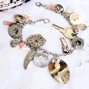 May include: A silver charm bracelet with a variety of pendants, including a key, a feather, a clock face, and a spoon-shaped charm with the text "Universal Studios". The bracelet also features pink beads and a button.