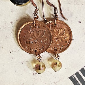 Peut inclure: Boucles d'oreilles en cuivre avec des pi&egrave;ces de monnaie canadiennes d'un cent avec un motif de feuille d'&eacute;rable et l'ann&eacute;e 2010. Chaque pi&egrave;ce est attach&eacute;e &agrave; une petite perle facet&eacute;e transparente.