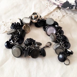 May include: A bracelet made of a silver chain with a variety of black, grey, and white buttons attached. The buttons are different shapes and sizes.