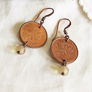 Peut inclure: Une paire de boucles d'oreilles en fil de cuivre et des pi&egrave;ces de monnaie canadiennes d'un cent de 2008 et 2010. Chaque pi&egrave;ce pr&eacute;sente un motif de feuille d'&eacute;rable et le mot "CANADA". Les boucles d'oreilles sont rehauss&eacute;es de petites perles de verre transparentes.