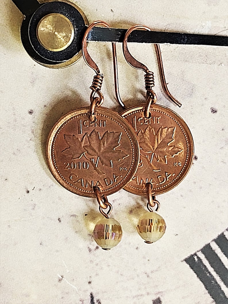 Peut inclure: Boucles d'oreilles en cuivre avec des pi&egrave;ces de monnaie canadiennes d'un cent avec un motif de feuille d'&eacute;rable et l'ann&eacute;e 2010. Chaque pi&egrave;ce est attach&eacute;e &agrave; une petite perle facet&eacute;e transparente.