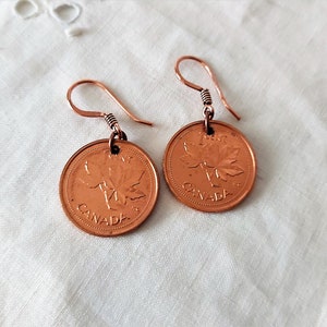 Peut inclure: Une paire de boucles d'oreilles en cuivre avec des pi&egrave;ces de monnaie canadiennes de 1 cent avec un motif de feuille d'&eacute;rable. Les pi&egrave;ces sont attach&eacute;es &agrave; de simples crochets en fil.