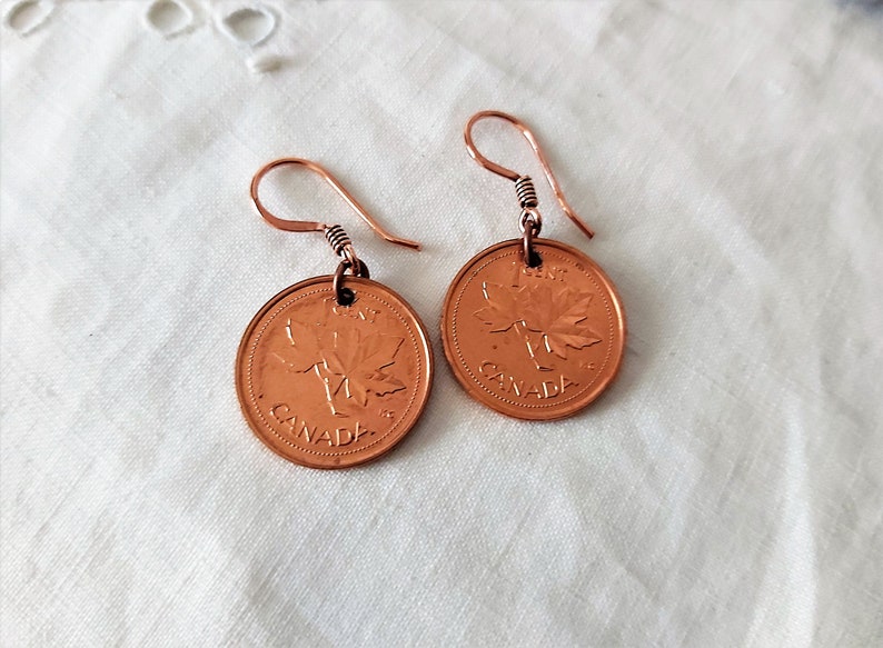 Peut inclure: Une paire de boucles d'oreilles en cuivre avec des pi&egrave;ces de monnaie canadiennes de 1 cent avec un motif de feuille d'&eacute;rable. Les pi&egrave;ces sont attach&eacute;es &agrave; de simples crochets en fil.