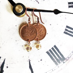 Peut inclure: Boucles d'oreilles en cuivre avec un sou canadien orn&eacute; d'un motif de feuille d'&eacute;rable et un pendentif en verre transparent. Le sou est dat&eacute; de 2010 et porte l'inscription "1 CENT" et "CANADA".