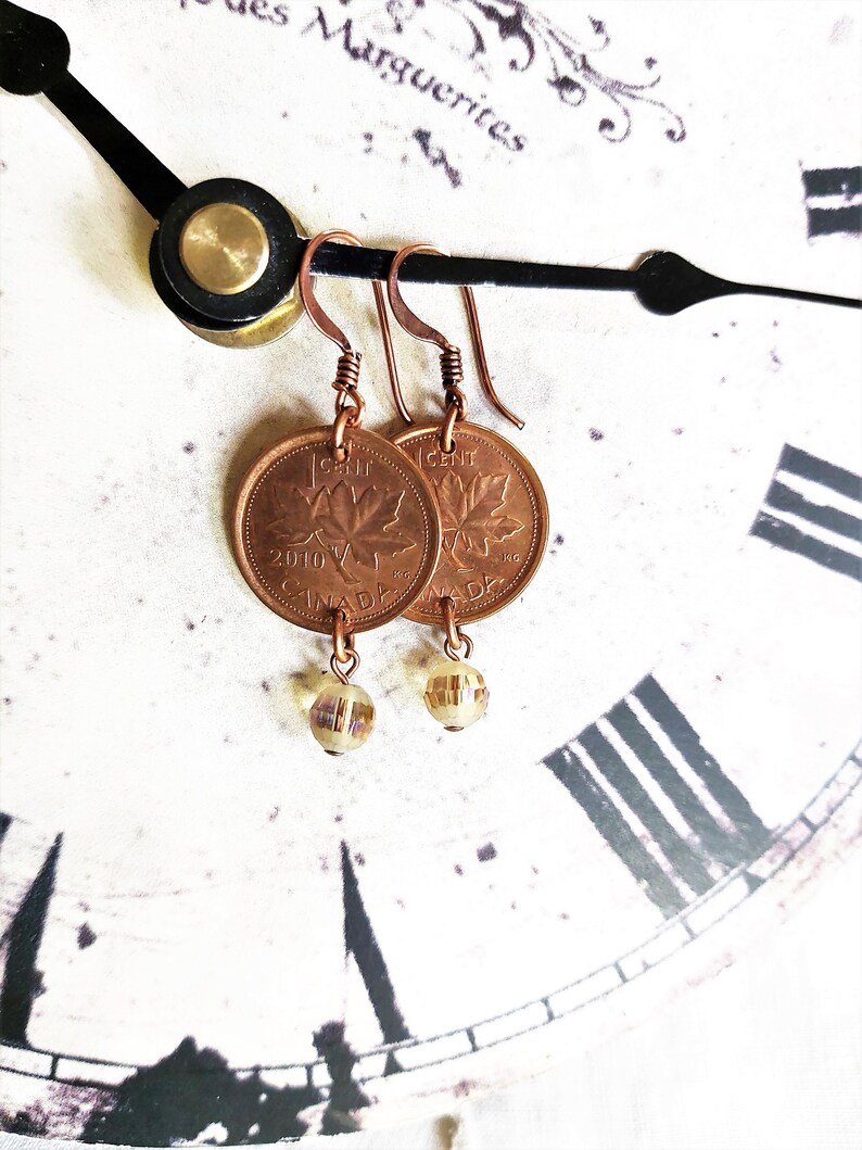 Peut inclure: Boucles d'oreilles en cuivre avec un sou canadien orn&eacute; d'un motif de feuille d'&eacute;rable et un pendentif en verre transparent. Le sou est dat&eacute; de 2010 et porte l'inscription "1 CENT" et "CANADA".