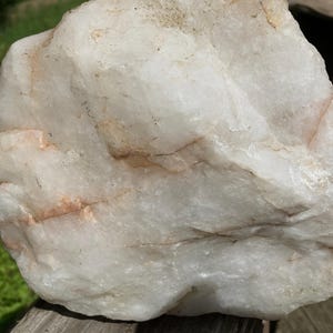 May include: A large, rough quartz rock, predominantly creamy white with delicate tan and peach-coloured veining. The surface has a textured appearance, with natural ridges and variations. Likely a decorative or collectible item, possibly for display.