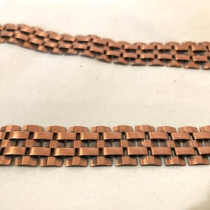 May include: Two copper-colored metal chain links are displayed against a light background. The chains have a rectangular, interlocking design. The chains are likely for a necklace or bracelet.