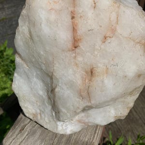 May include: A large, irregularly shaped quartz rock. The rock has a creamy white base colour with reddish-brown veining. It has a rough, textured surface and is displayed outdoors.