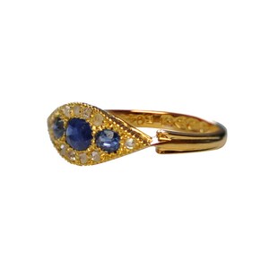 Op de afbeelding: Een gouden ring met een driehoekige band bezet met drie blauwe saffieren en kleine witte diamanten.