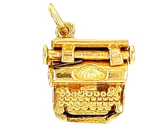 May include: A gold-colored charm in the shape of a vintage typewriter. The charm has a detailed design with a carriage return lever, keys, and a paper roller.