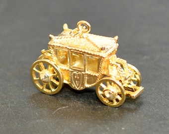 Puede incluir: Un amuleto de carruaje de color dorado con detalles intrincados. El amuleto presenta un diseño detallado de un carruaje tirado por caballos con cuatro ruedas y un techo. El carruaje está hecho de metal y tiene un acabado brillante.