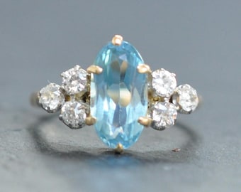 May include: A gold ring with a large oval-shaped blue gemstone surrounded by smaller round white gemstones.