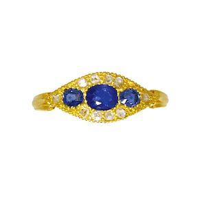 Op de afbeelding: Een gouden ring met drie blauwe saffieren en een halo van kleine diamanten.
