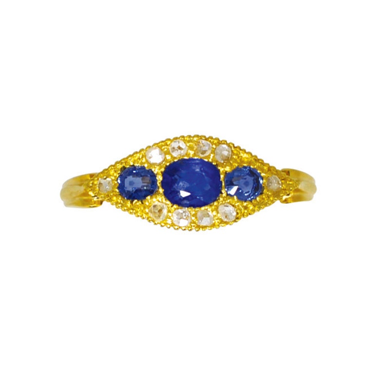 Op de afbeelding: Een gouden ring met drie blauwe saffieren en een halo van kleine diamanten.