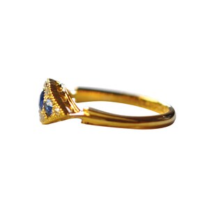 Op de afbeelding: Een gouden ring met een driehoekige zetting met een cluster van blauwe saffieren en kleinere witte diamanten.