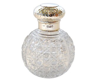 May include: A clear glass bottle with a silver top and a textured design. The bottle is round and has a small opening at the top. The silver top has a hammered finish.