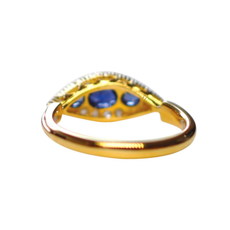 Op de afbeelding: Een gouden ring met een blauwe saffier en diamant accenten. De ring is gezet in een delicaat, ingewikkeld ontwerp.