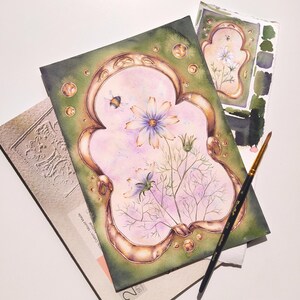 May include: Watercolor painting of a cosmos flower with a bumblebee, framed in a gold-colored ornate border. The painting is on a green background with gold accents. A paintbrush and a color palette are also visible.