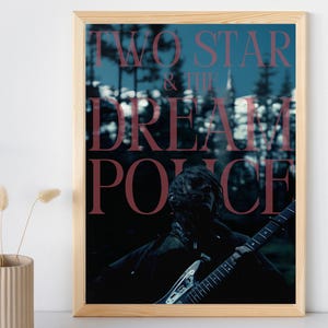 Op de afbeelding: Een ingelijst afdruk van een band genaamd "Two Star & The Dream Police". De afdruk toont een persoon die een gitaar vasthoudt voor een wazige bosachtergrond.