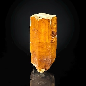May include: A large, translucent, orange-brown crystal with striations and a pointed tip. The crystal is sitting on a black surface.