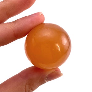 May include: A smooth, polished orange carnelian sphere. The sphere is about the size of a golf ball and has a warm, inviting color.