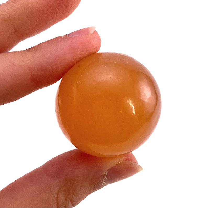 May include: A smooth, polished orange carnelian sphere. The sphere is about the size of a golf ball and has a warm, inviting color.
