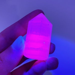 May include: A pink crystal point with a layered appearance, glowing under a UV light.