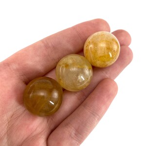 K&ouml;nnte beinhalten: Drei gelbe Citrin-Kristallkugeln, jede mit einer glatten, polierten Oberfl&auml;che. Die Kugeln sind durchscheinend und haben einen leicht goldenen Farbton.