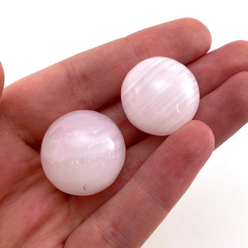 May include: Two smooth, white selenite spheres with a striated pattern. The spheres are approximately 2 inches in diameter.