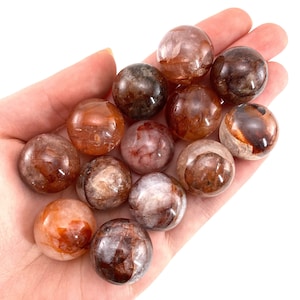 Op de afbeelding: Een verzameling van 12 kleine, ronde, doorschijnende, bruine en oranje kristallen bollen.
