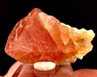 Puede incluir: Un gran cristal de color rojo anaranjado con un aspecto translúcido y vítreo. El cristal tiene una forma angular y afilada con múltiples facetas.