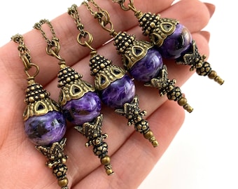 May include: Five purple and gold pendant necklaces with ornate metal accents. Each pendant features a round, purple stone with a swirling pattern.
