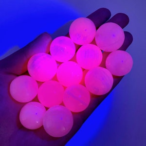 May include: A collection of 12 pink and white glowing spheres, likely made of selenite or calcite, arranged in a hand. The spheres are smooth and translucent, with a slight shimmer.
