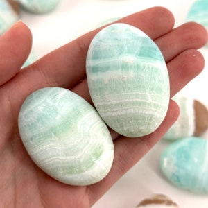 Op de afbeelding: Twee gladde, ovale groene en witte celestiet palmstenen. De stenen hebben een gebandeerd patroon en zijn gepolijst.
