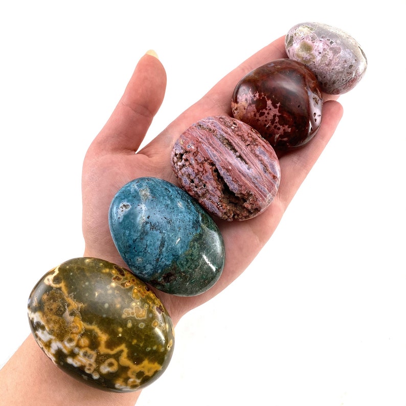 May include: Five smooth, polished, oval-shaped stones in various colours and patterns. The stones are arranged in a row, with the largest stone at the bottom and the smallest stone at the top. The stones are a variety of colours, including green, blue, red, and brown.