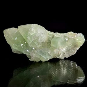May include: A cluster of pale green crystals with a reflective surface. The crystals have a translucent quality, with sharp edges and varying sizes. The overall shape is irregular, with multiple points and facets.