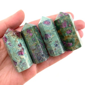 May include: Four green and pink ruby in zoisite crystal points, also known as ruby zoisite, are arranged in a row. The points are polished and have a smooth, glassy finish.