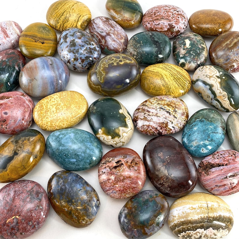 May include: A collection of 20 tumbled stones in various colours and patterns, including green, blue, red, yellow, and brown. The stones are smooth and polished, and they are arranged in a random pattern on a white background.