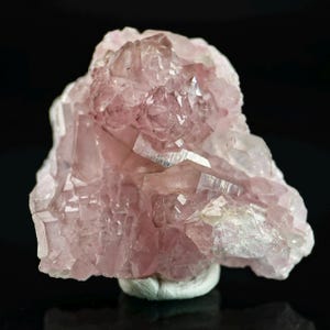 May include: A cluster of pink quartz crystals with a crystalline structure. The quartz has a translucent appearance with variations in color, ranging from pale to deeper shades of pink. The crystals are mounted on a white base.