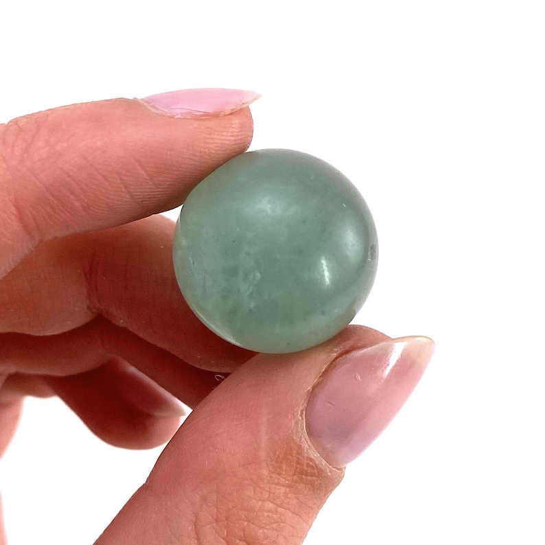 May include: A smooth, green sphere made of polished stone. The sphere is about the size of a golf ball and has a translucent quality.