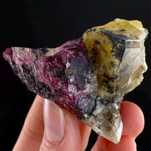 Może przedstawiać: Naturalny okaz minerału z kombinacją kolorów. Kawałek prezentuje żywą mieszankę głębokiej magenty, żółci i przezroczystych formacji kryształowych. Minerał ma szorstką, teksturowaną powierzchnię z obszarami czarnymi i szarymi.
