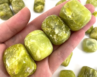 May include: A collection of green serpentine tumbled stones. The stones are smooth and polished, with a variety of green shades and patterns.