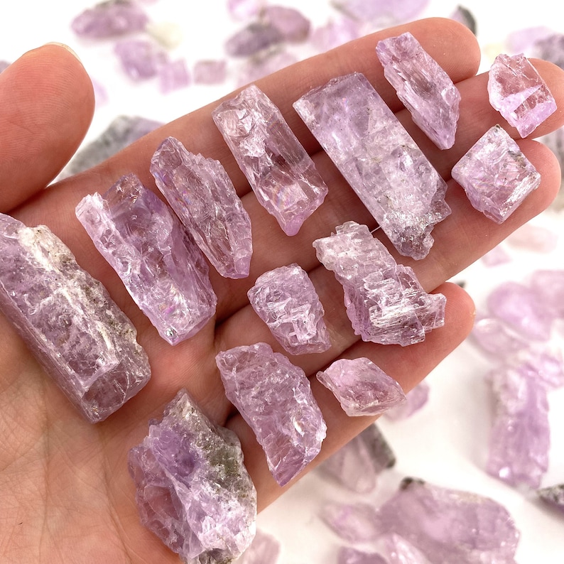K&ouml;nnte beinhalten: Eine Sammlung kleiner, roher, rosa und violetter Selenitkristalle. Die Kristalle sind in verschiedenen Formen und Gr&ouml;&szlig;en und haben eine nat&uuml;rliche, raue Textur.