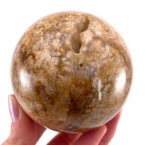 May include: A large, brown and white agate sphere with a natural crack and a small hole. The sphere is polished and has a smooth, glossy finish.
