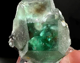 Könnte beinhalten: Ein großer, grüner Fluoritkristall mit einem klaren, glasartigen Aussehen. Der Kristall hat eine komplexe, vielseitige Struktur mit mehreren sichtbaren Facetten. Der Kristall ist teilweise durchscheinend, sodass Licht hindurchscheinen kann.