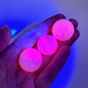 May include: Three pink and white spheres with a marbled appearance, glowing under a UV light.