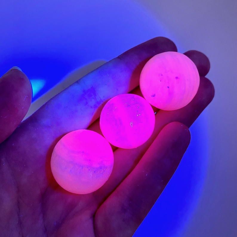 May include: Three pink and white spheres with a marbled appearance, glowing under a UV light.