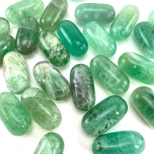 May include: A collection of green fluorite tumbled stones. The stones are smooth and polished, with a variety of shades of green.