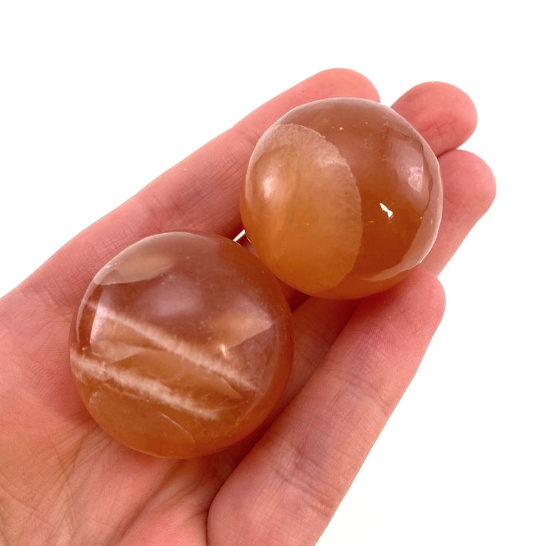May include: Two orange calcite spheres with white striations. The spheres are smooth and polished.
